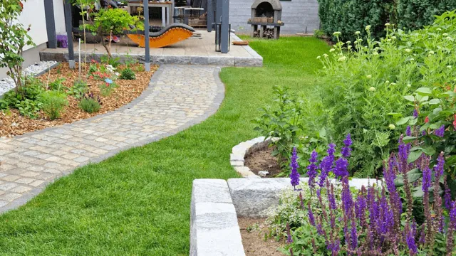 Angelegter Garten mit gepflastertem Weg, Rasenfläche und lila blühenden Stauden